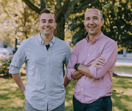 Own Up Co-founders Patrick and Mike stand side by side in a park and smile at the camera