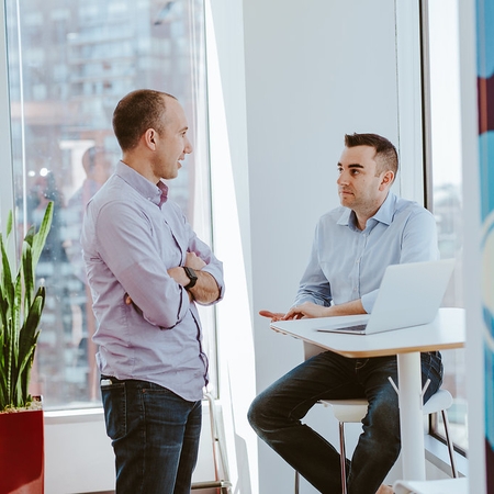 Own Up Co-founders Patrick and Mike chat at a hightop table in a bright room filled with sunlight